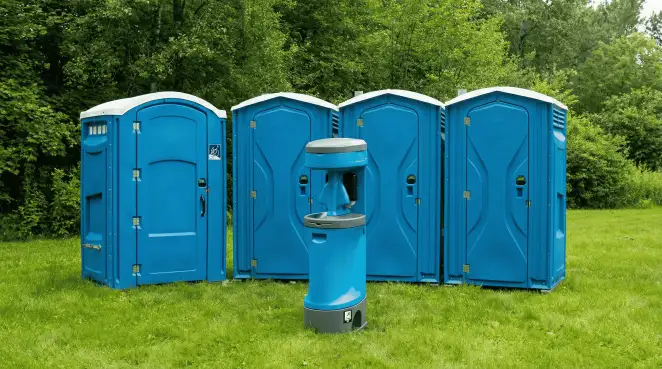 Four blue portable toilets and a matching hand washing station on grass near trees, a common sight at local outdoor events in Pueblo, CO