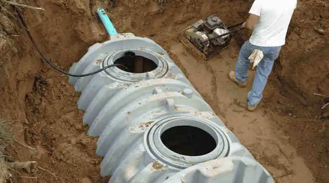 Septic tank installation showing a technician compacting soil around a new poly septic tank in an excavation pit in Pueblo, CO